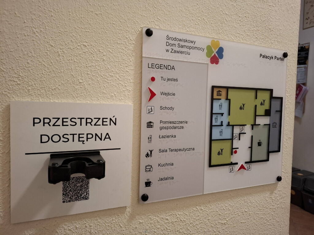 Tyfloplan parteru z legendą, oznaczeniami pomieszczeń i punktem „Tu jesteś”.