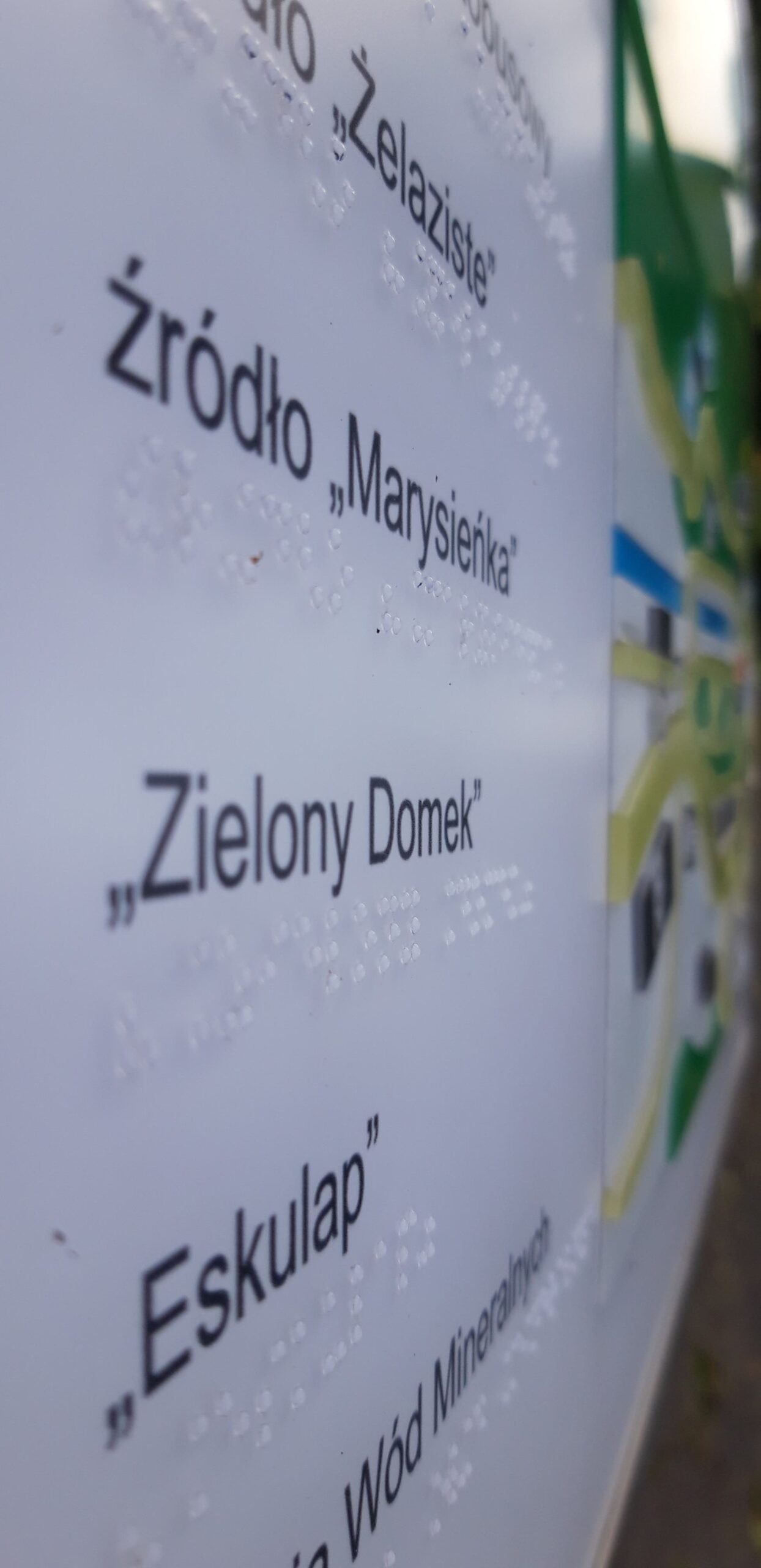 Tablica informacyjna z napisami w alfabecie Braille’a, zawierająca nazwy źródeł finansowania, m.in. „Źródło »Marysieńka«”, „Zielony Domek” i „Eskap”.