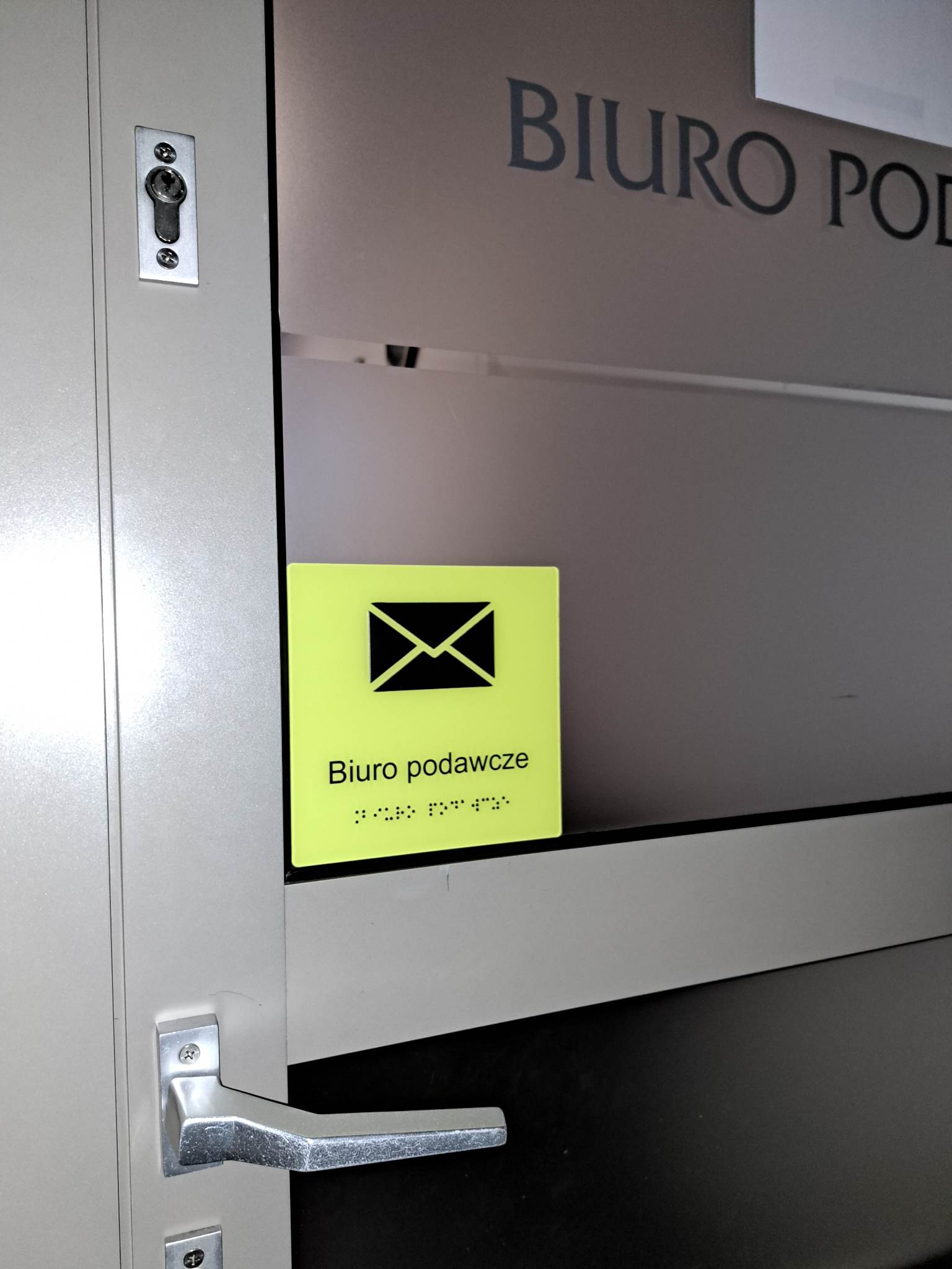 Tabliczka „Biuro podawcze” z symbolem koperty i napisem w alfabecie Braille’a.
