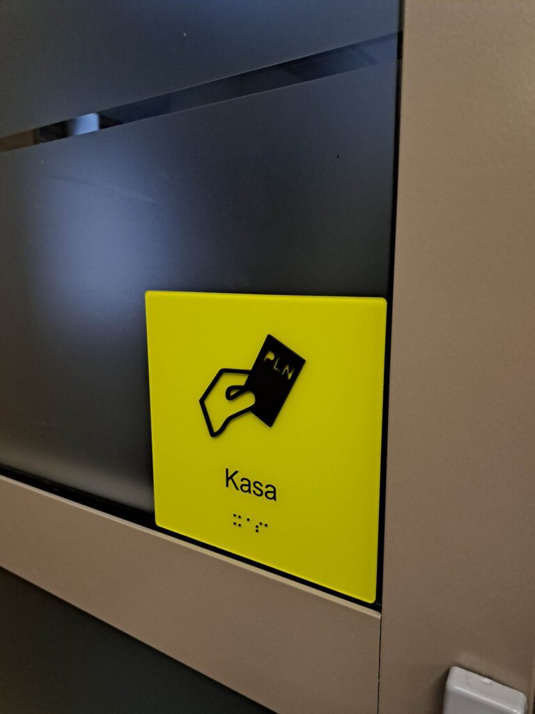 Tabliczka „Kasa” z symbolem karty płatniczej i napisem w alfabecie Braille’a.