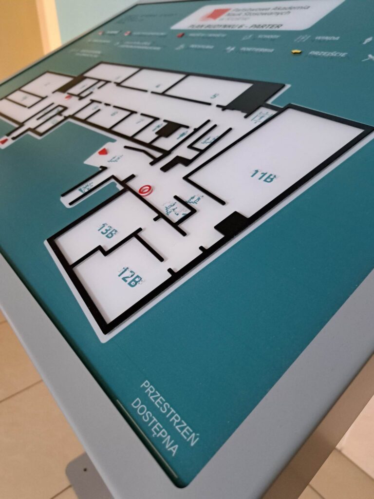Plan tyflograficzny budynku z oznaczeniami pomieszczeń, ciągów komunikacyjnych, schodów i wyjść ewakuacyjnych, wykonany w formie wypukłej z opisami w brajlu.