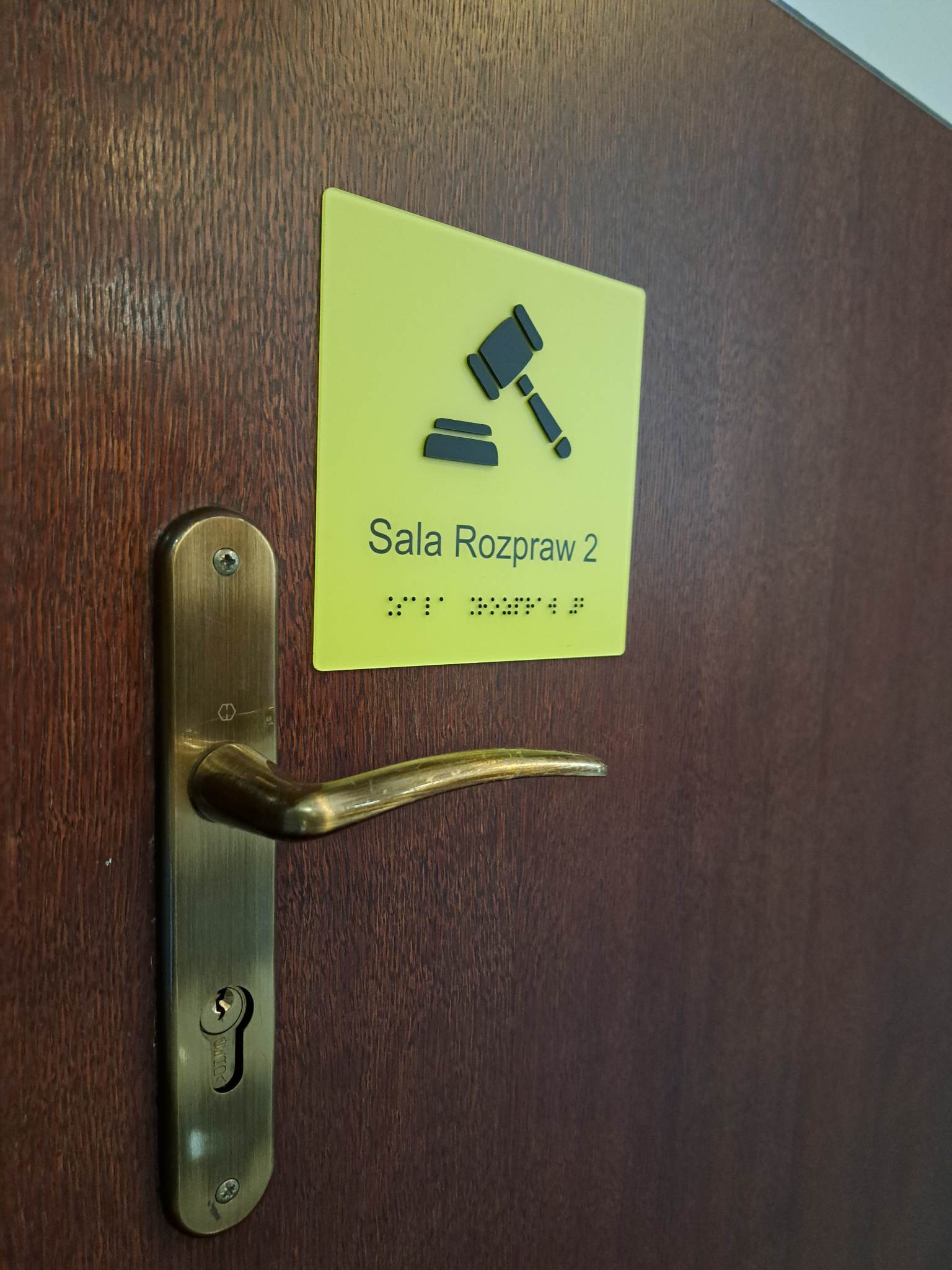 Tabliczka „Sala Rozpraw 2” z oznaczeniem sali i napisem w alfabecie Braille’a.