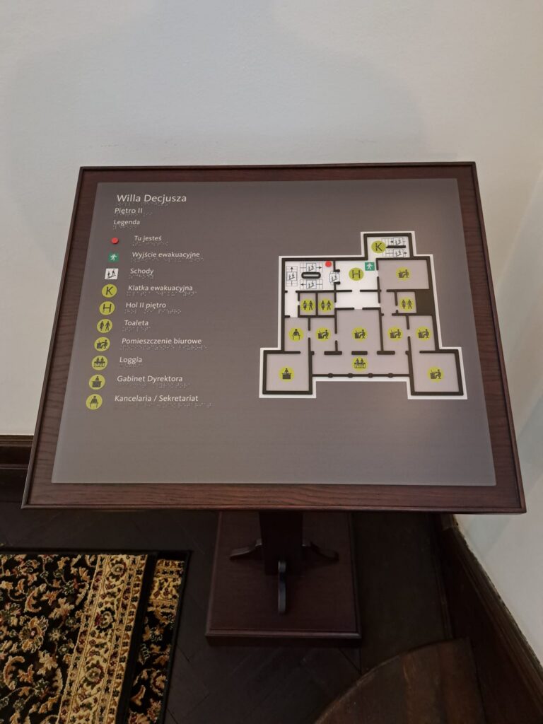 Plan tyflograficzny Willi Decjusza – piętro II z oznaczeniami pomieszczeń i wyjść ewakuacyjnych.