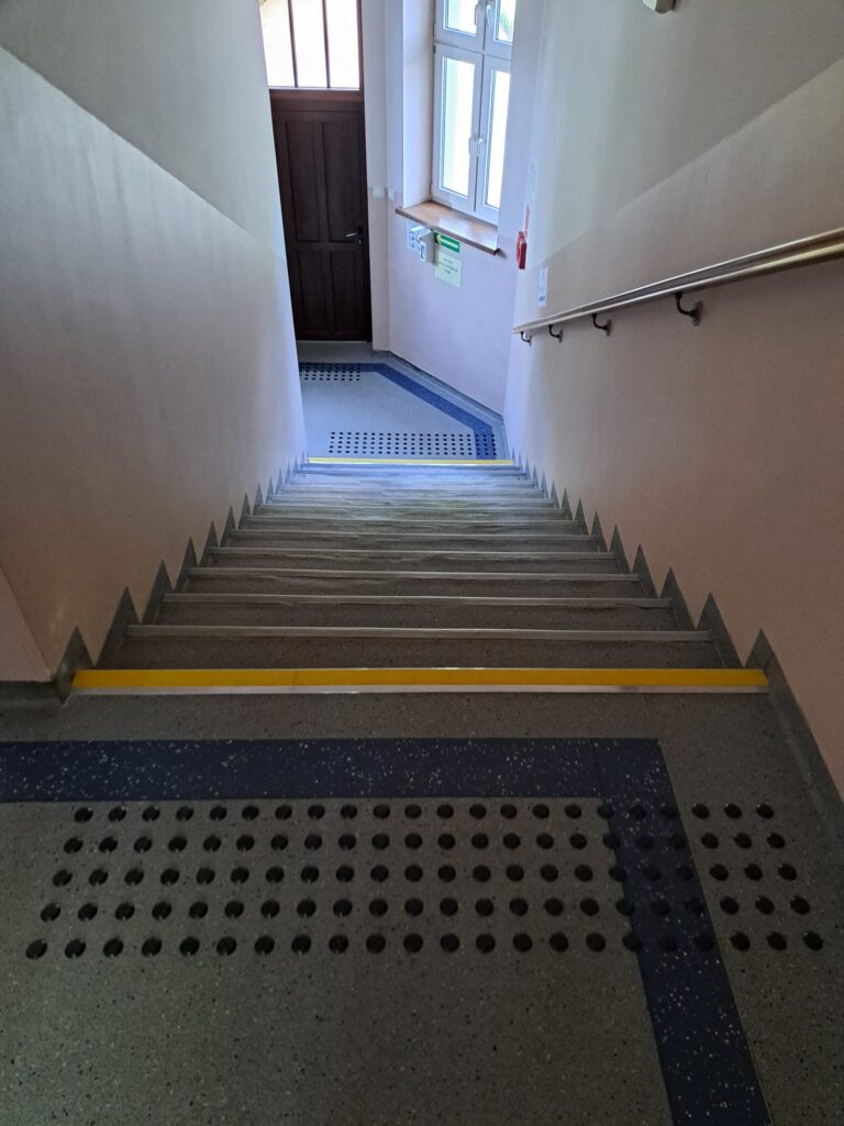 Schody z kontrastowymi oznaczeniami stopni i polami uwagi.