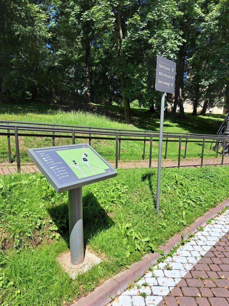 Zdjęcie przedstawiające mapę zespołu pałacowo-parkowego Willa Decjusza i drogowskaz.