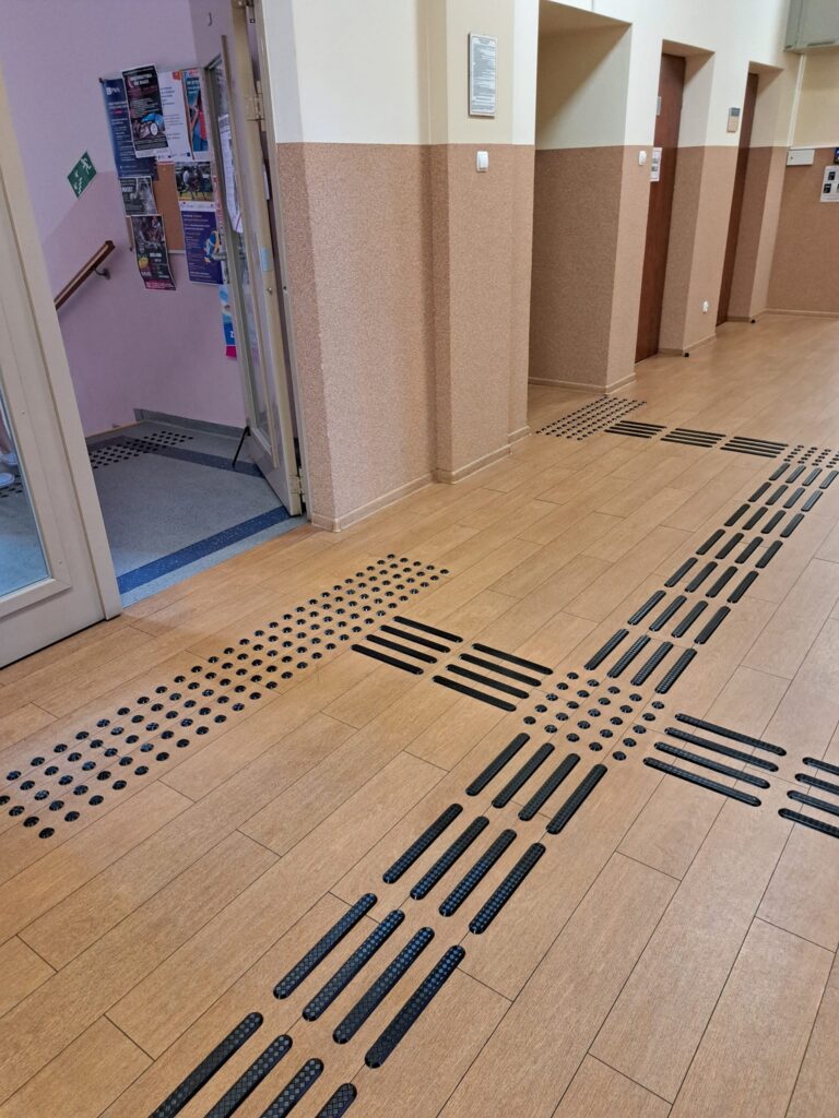 Korytarz z dotykową ścieżką prowadzącą i polami uwagi.