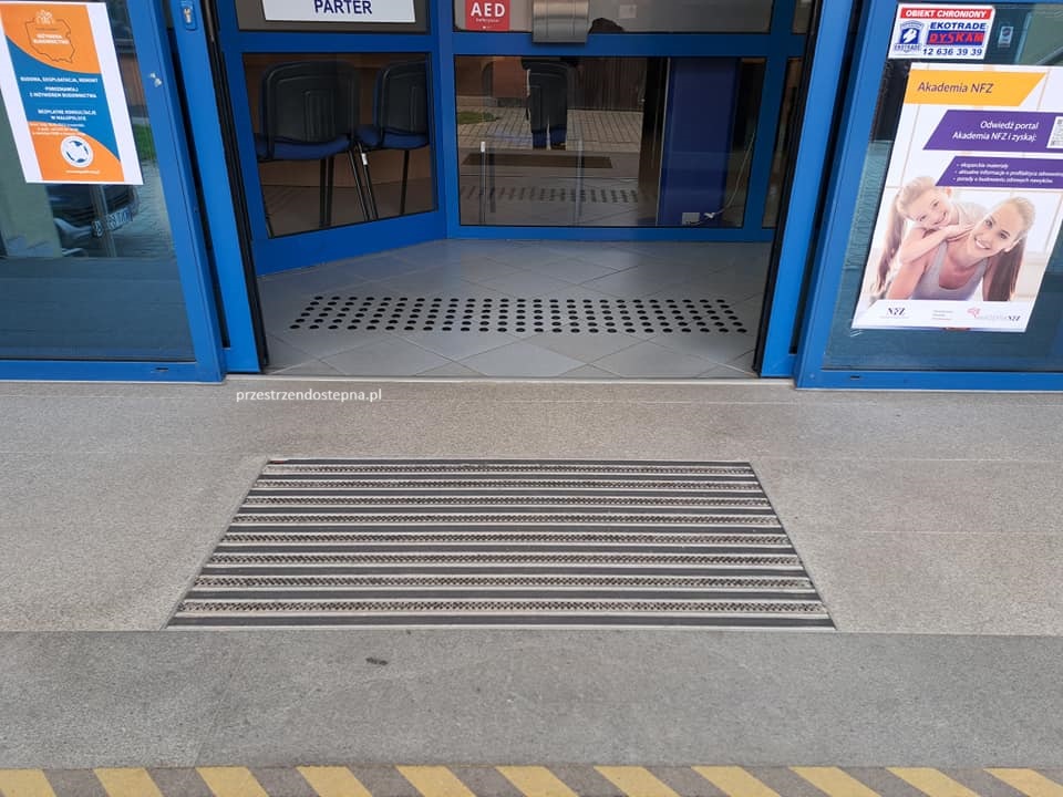 Mata wejściowa z polami prowadzącymi i ostrzegawczymi przed wejściem do budynku.