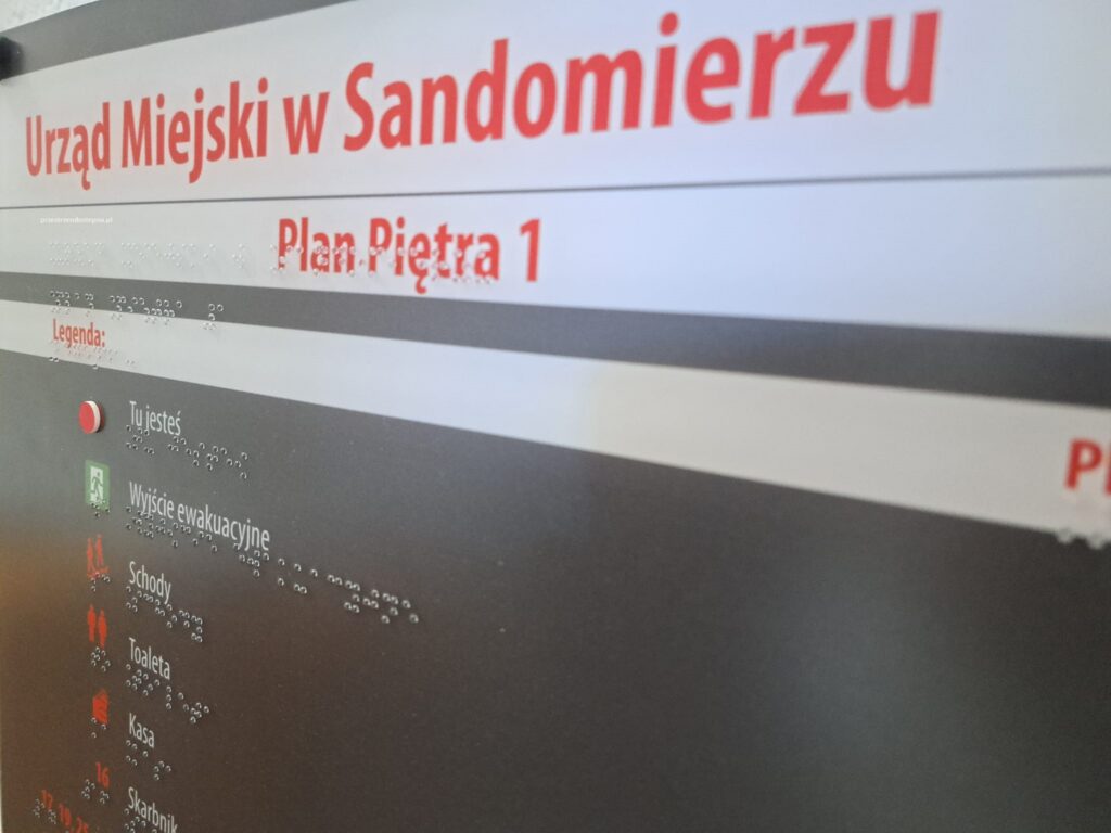Tablica informacyjna Urzędu Miejskiego w Sandomierzu z planem piętra, legendą i oznaczeniami w alfabecie Braille’a.