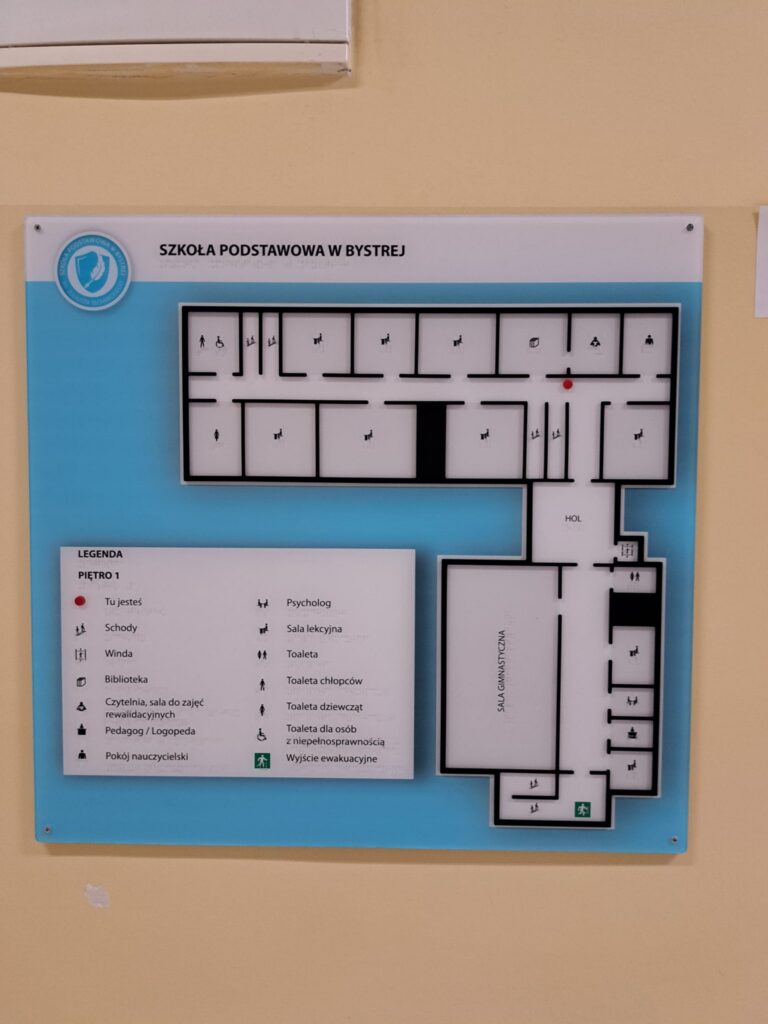 Tyflograficzna mapa Szkoły Podstawowej w Bystrej z legendą, oznaczeniami pomieszczeń i wyjść ewakuacyjnych.