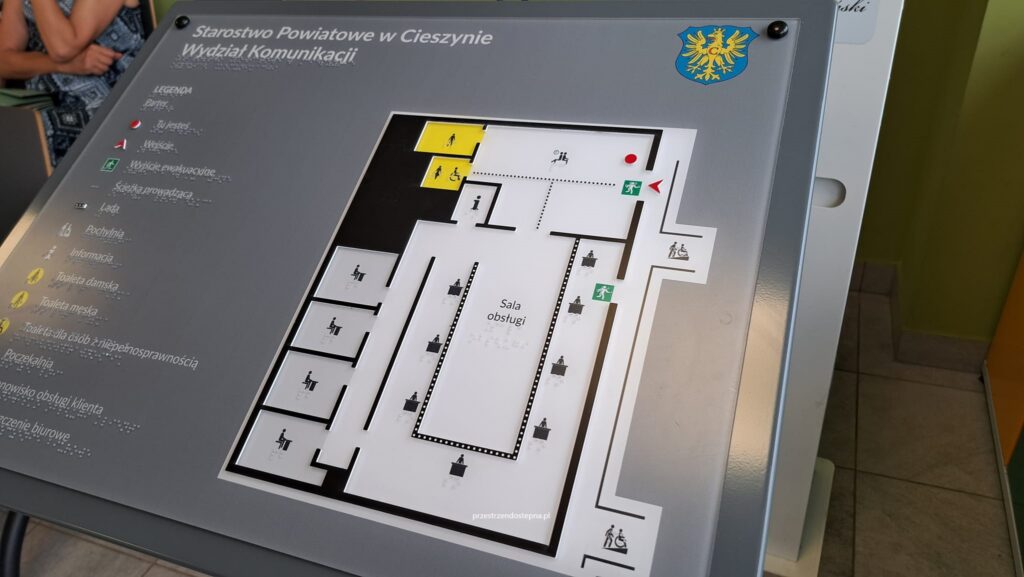 Dotykowy plan orientacyjny Starostwa Powiatowego w Cieszynie – Wydziału Komunikacji, z legendą w alfabecie Braille’a oraz wypukłym planem pomieszczeń.