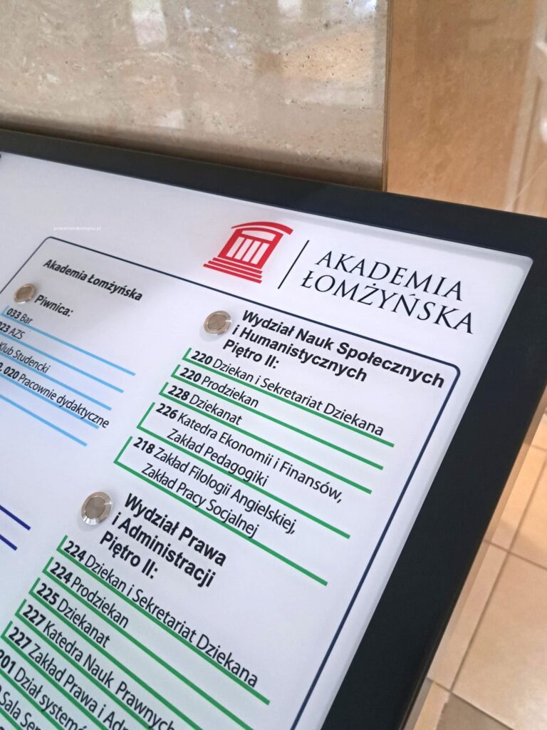 Tablica tyflograficzna z planem piętra Akademii Łomżyńskiej, z oznaczeniami pomieszczeń, wind, schodów i toalet w brajlu.
