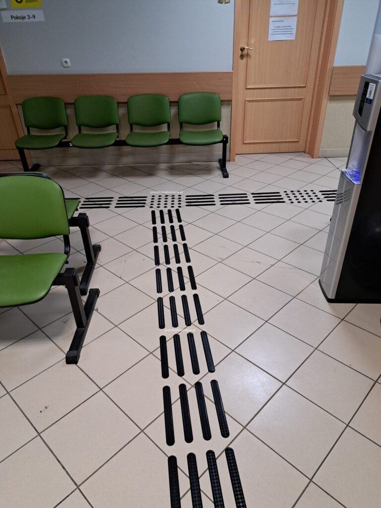 Ścieżka dotykowa z polem uwagi prowadząca przez poczekalnię.
