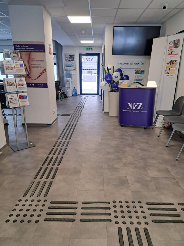 Punkt obsługi klienta NFZ z dotykową ścieżką prowadzącą do stanowiska obsługi.