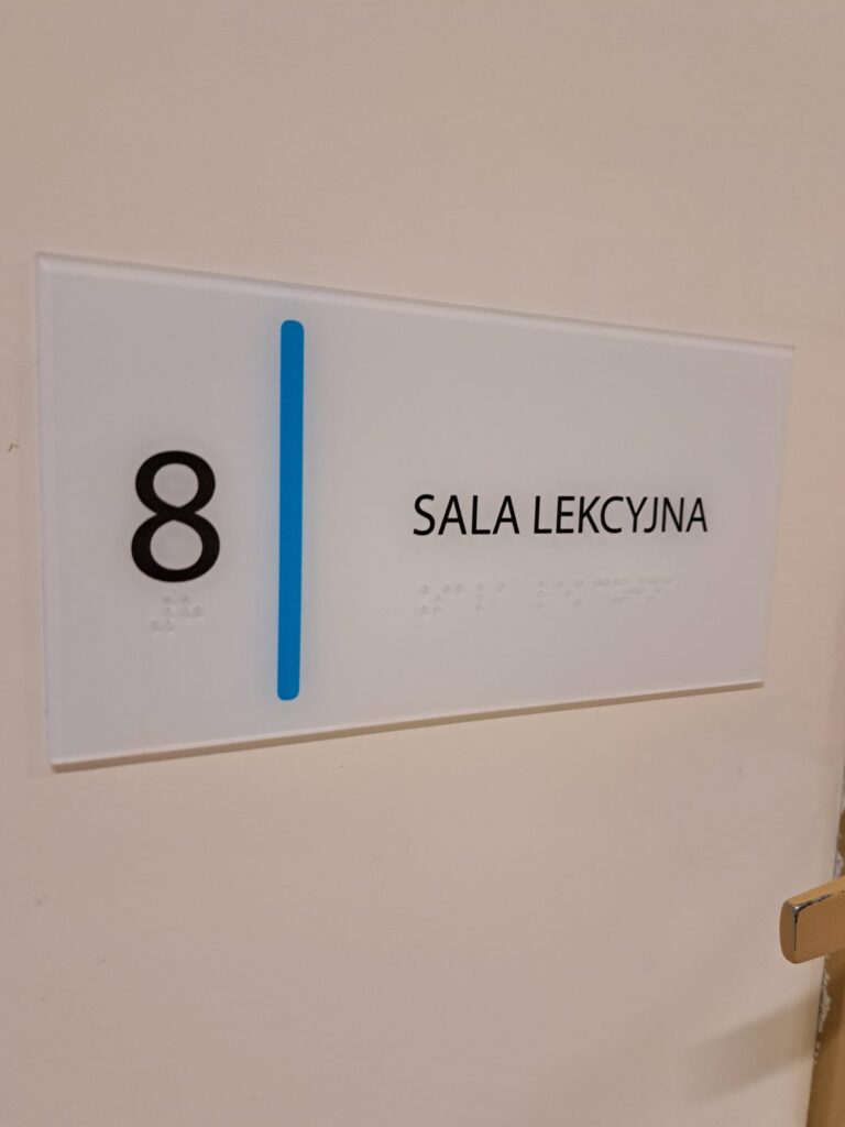 Tabliczka z numerem 8 i napisem „Sala lekcyjna” oraz oznaczeniem w alfabecie Braille’a.